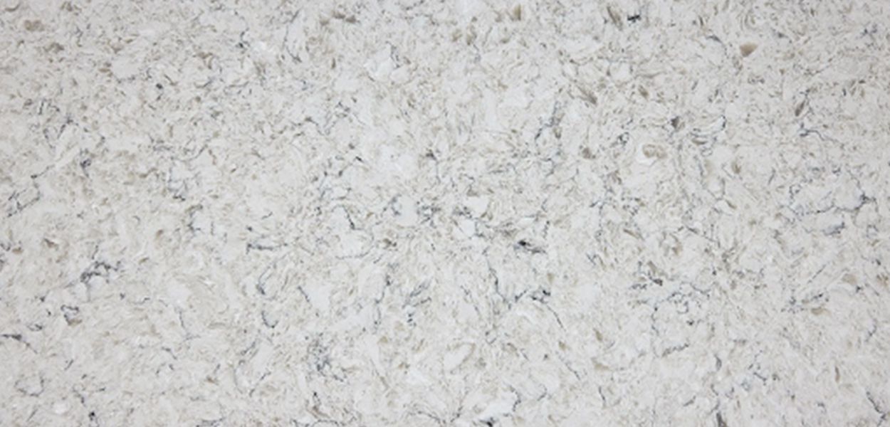 A close-up view of white quartz countertop material with a fine, light grey marbled and speckled texture.