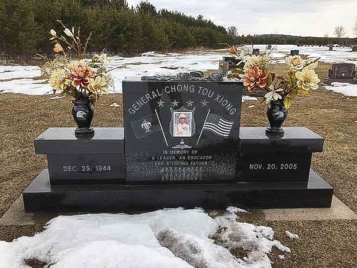Tombstone for General Chong Tou Xiong in a snow-covered cemetery, flanked by vases of flowers.
