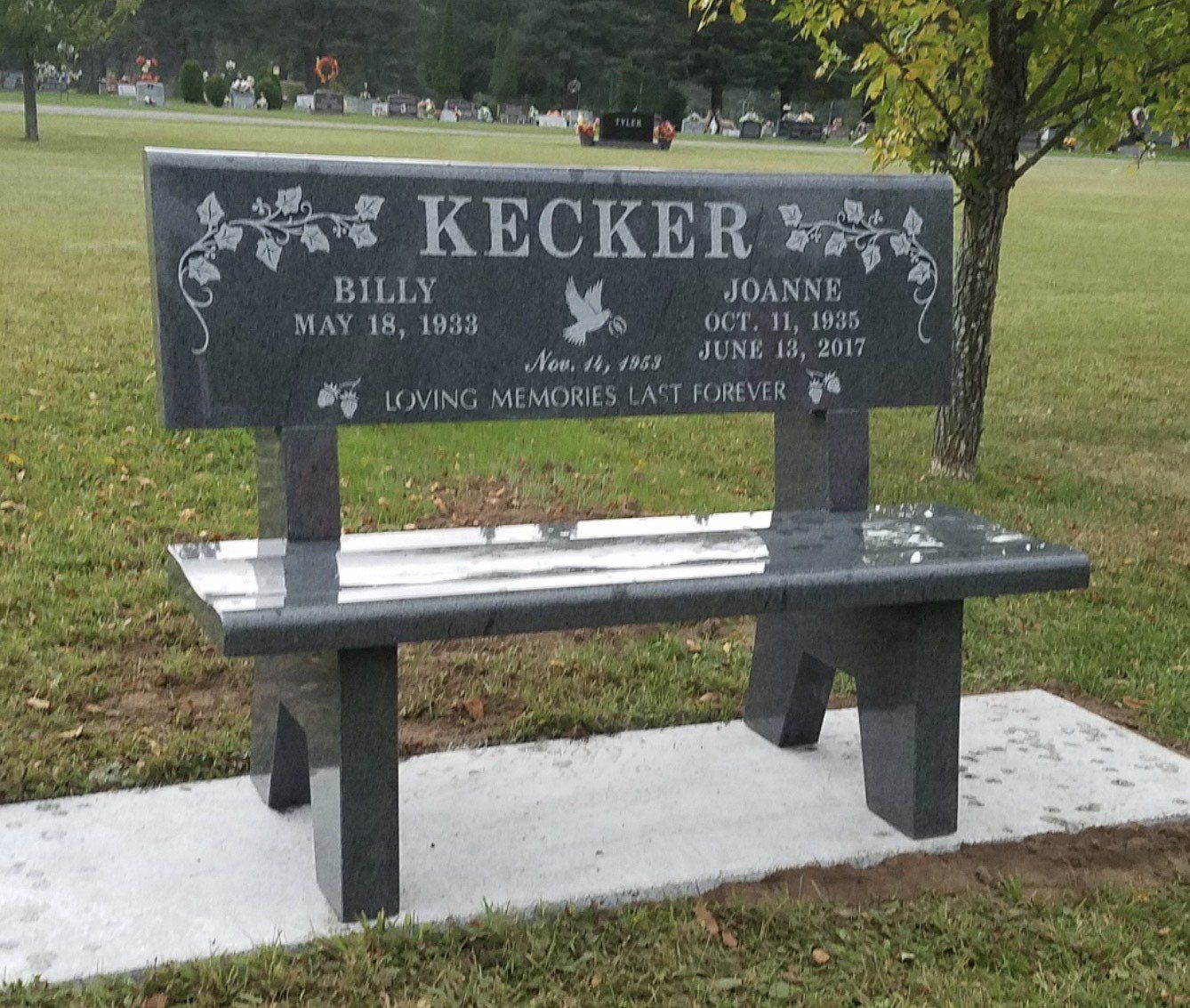 Granite bench memorial with engraved names and dates in a cemetery.