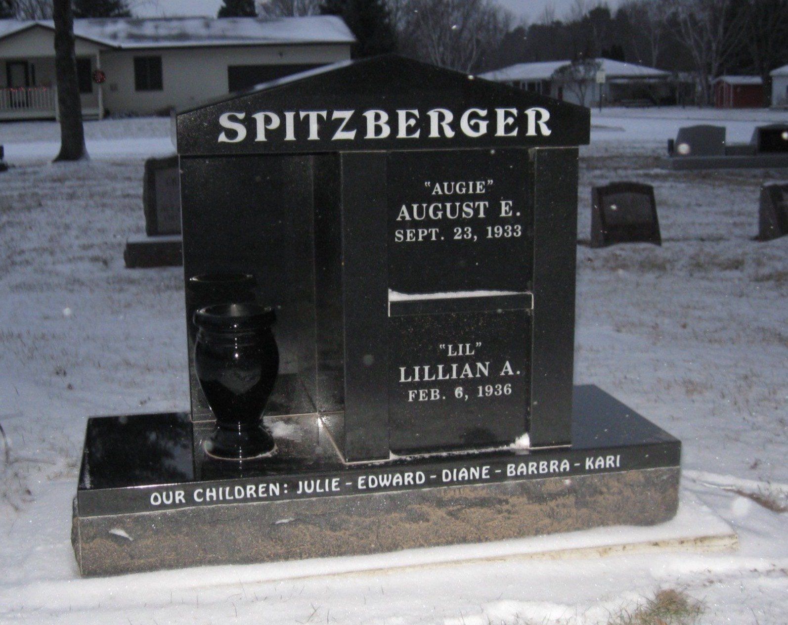 Black granite headstone in a snowy cemetery. It is inscribed with the 