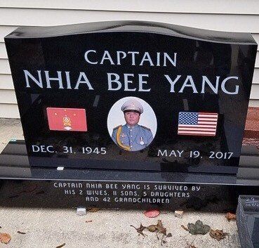Headstone of Captain Nhia Bee Yang, with photo, dates 1945-2017, flags, and inscription mentioning family.
