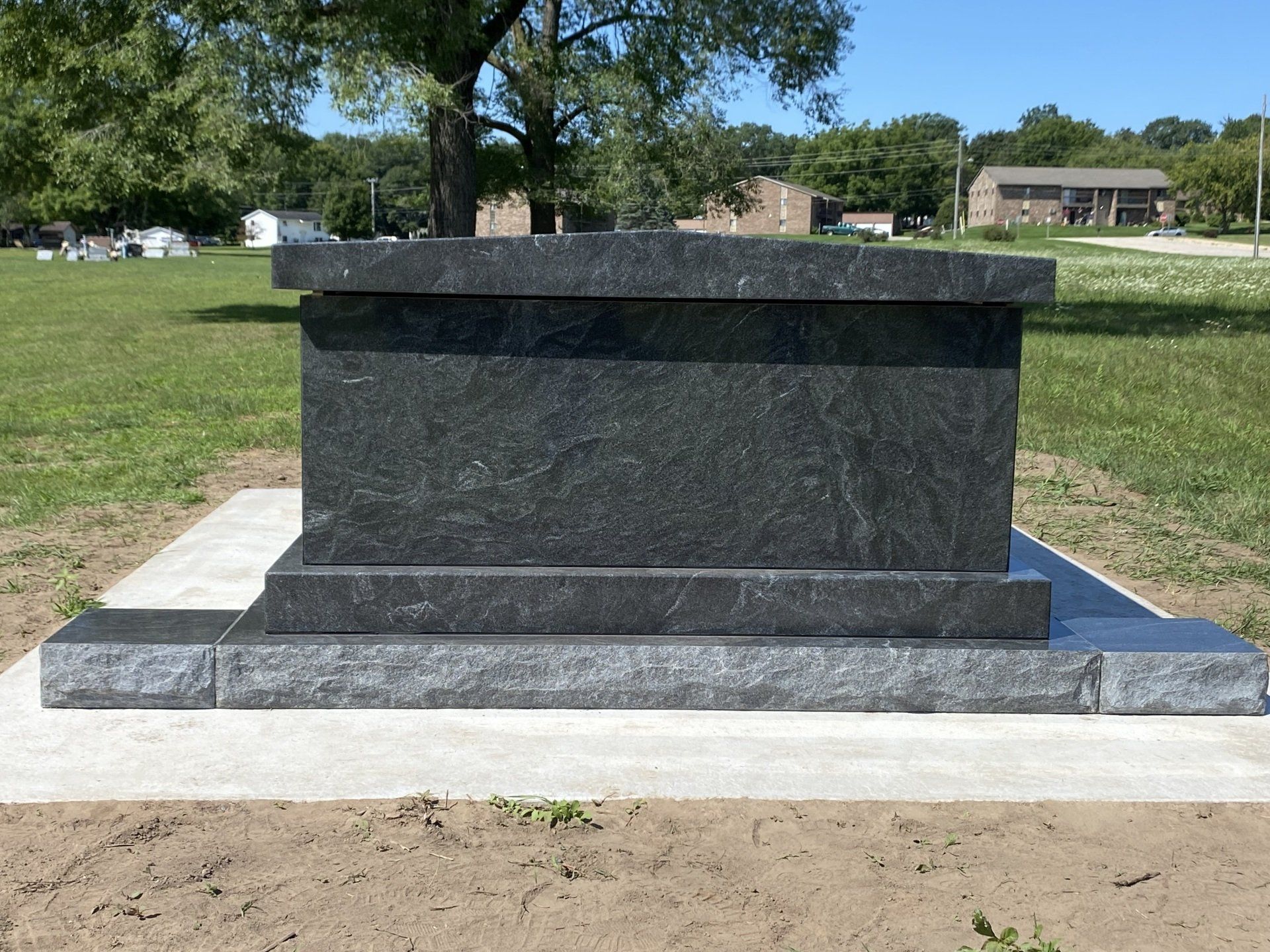 Dark gray granite tombstone on a light gray concrete base, outdoors.