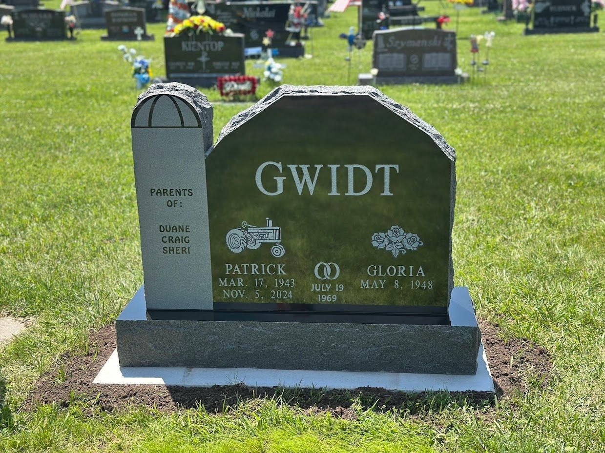 Headstone: GWIDT, green, tractor, clover, Patrick & Gloria, gray base in grassy cemetery.