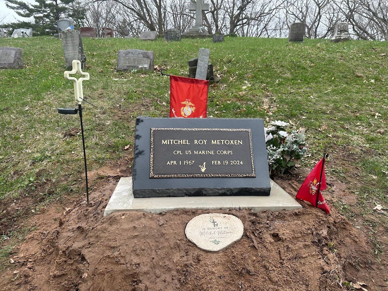 Grave with headstone honoring Michael Roy Wallace, with cross, flags, and green grass in a cemetery.