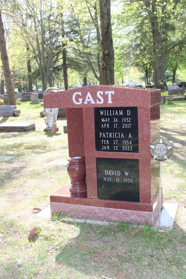 Red granite Gast family headstone in a cemetery with names and dates.