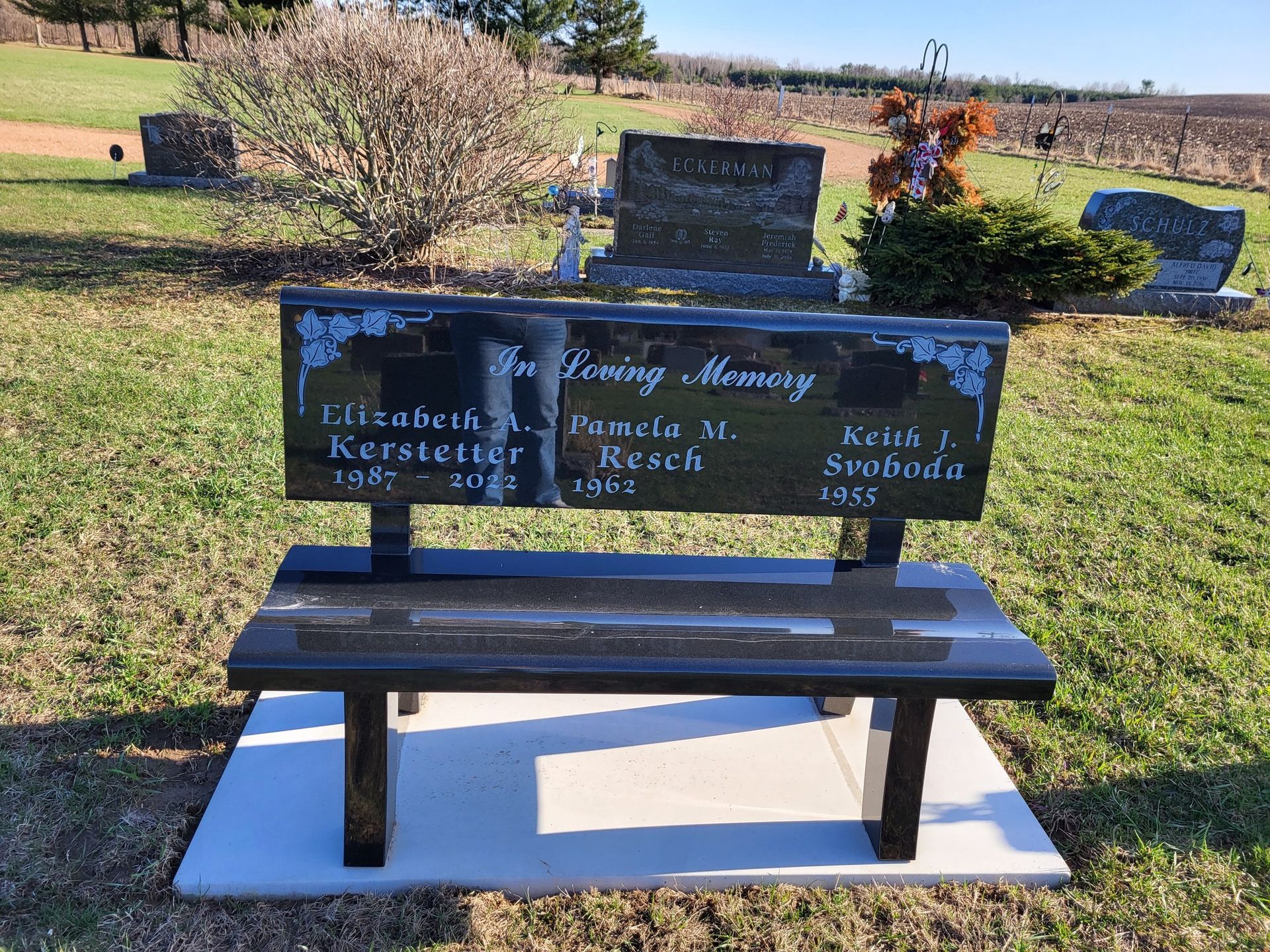 Black memorial bench in a cemetery with names inscribed.