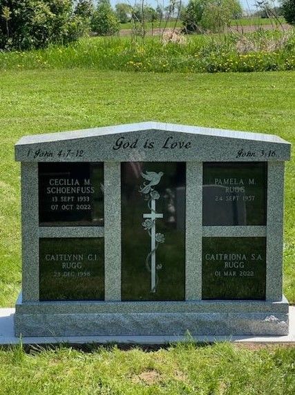 Granite family tombstone with names, dates, and cross etched on a sunny, grassy lawn.