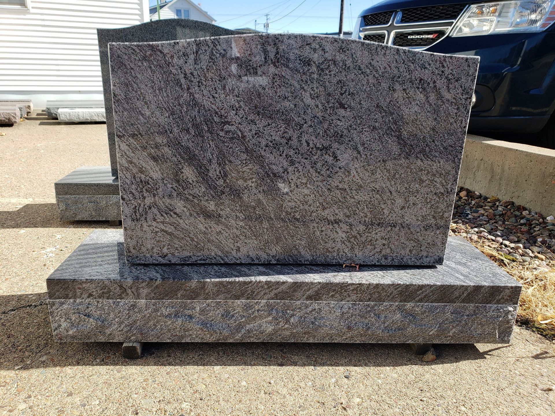 A granite headstone in shades of gray, sitting on a rectangular base, outdoors.