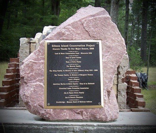 Monument with a plaque, honoring donors to a conservation project. Set outdoors with trees; red-brown stone and brick.