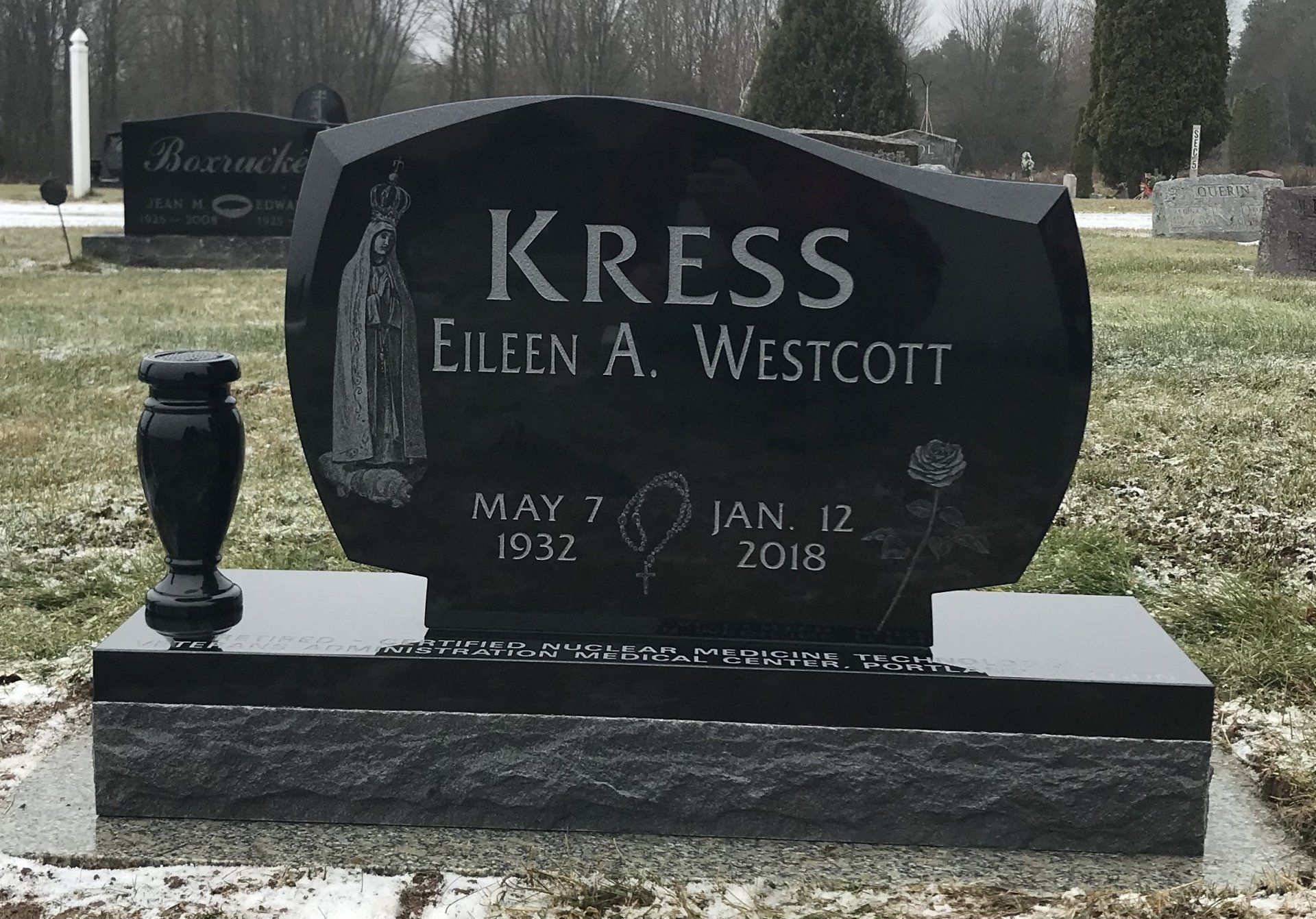 Black headstone with the name Kress and dates; a vase is to the left.