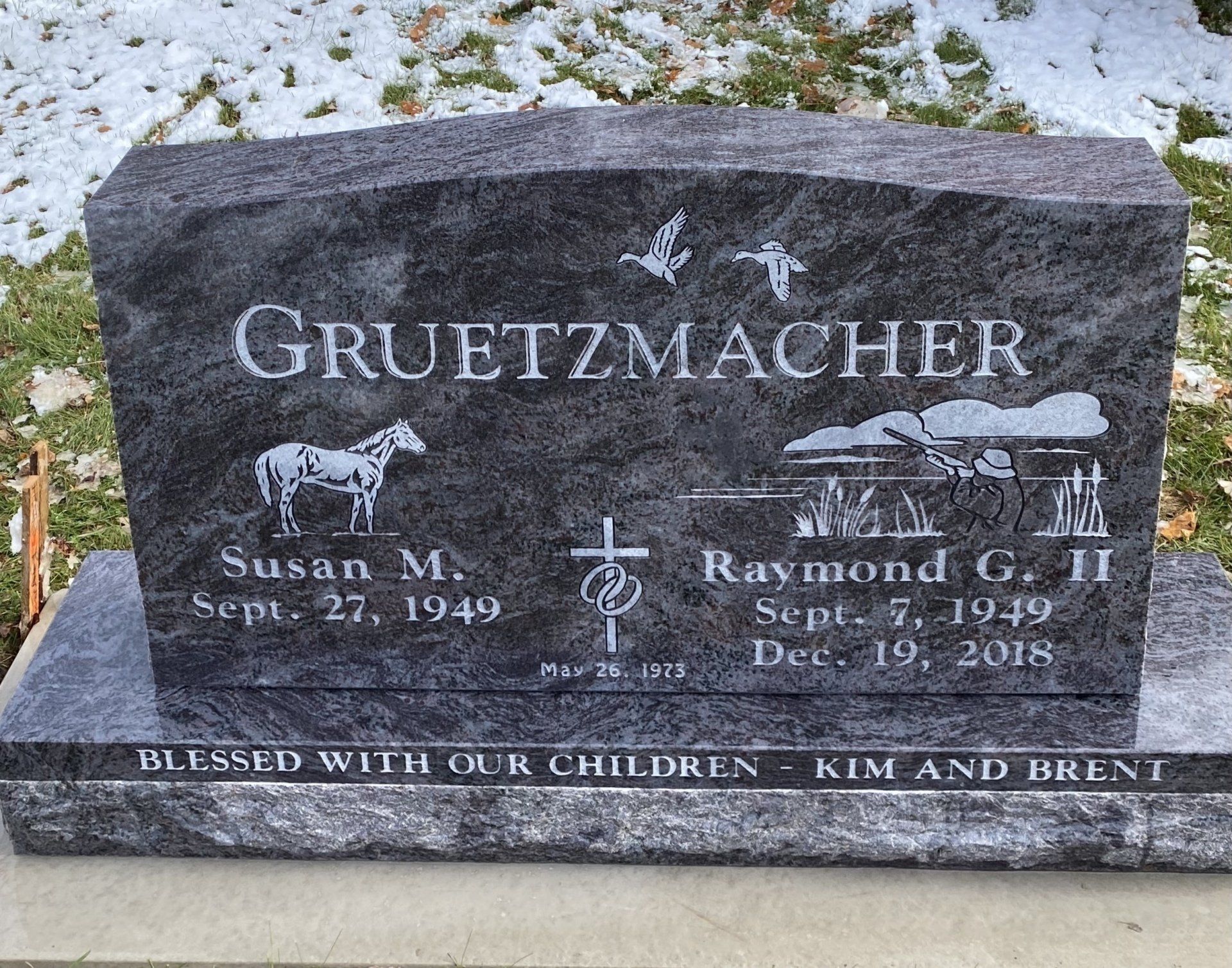 Gray granite headstone with Gruetzmacher family details, horse, cross, birds, landscape; includes dates and names.
