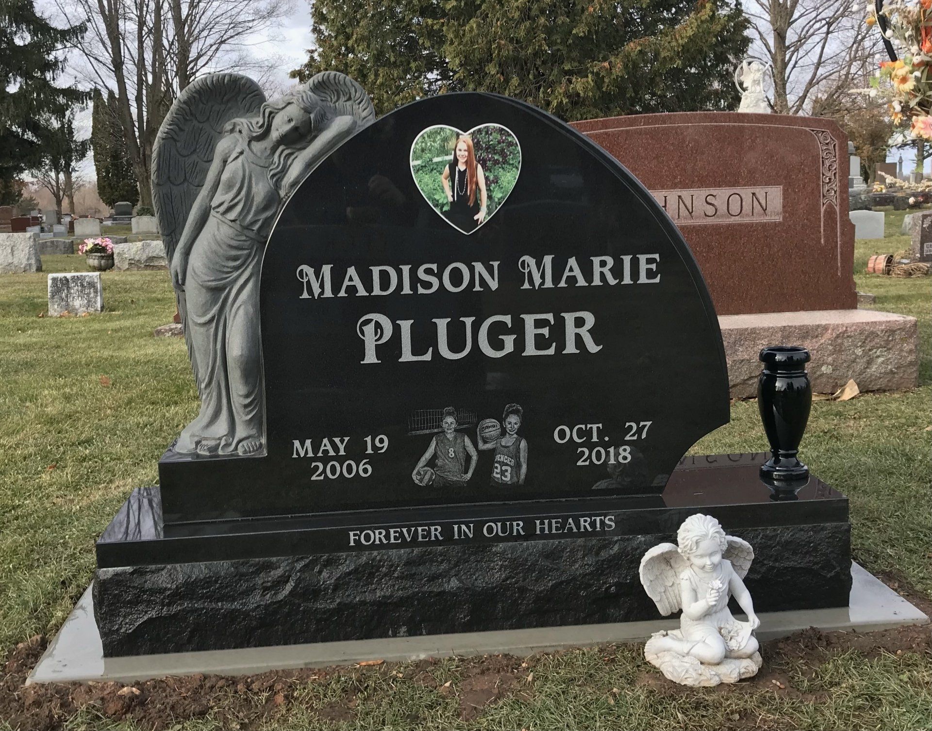 Black granite headstone with angel sculpture, photo, and inscription for Madison Marie Pluger in a cemetery.