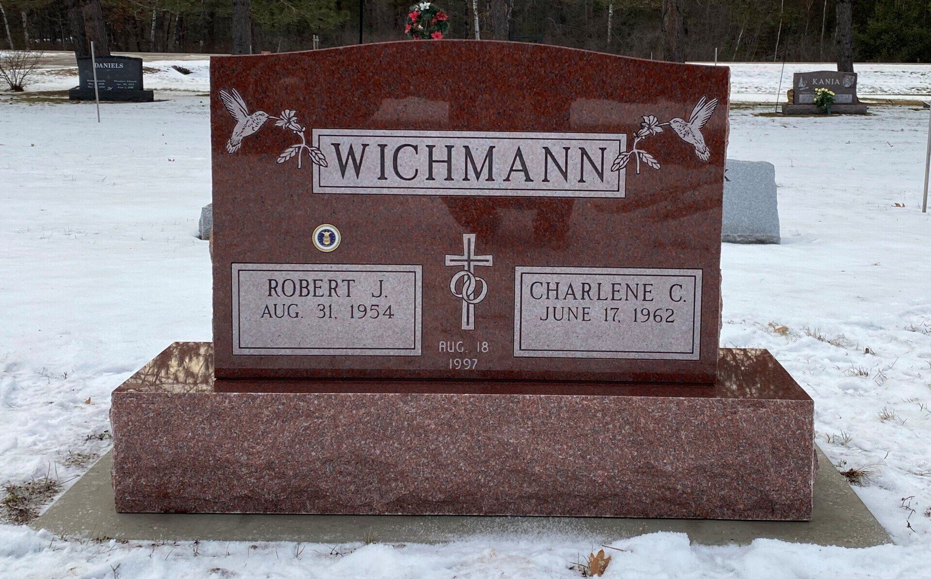Red granite headstone in snowy cemetery, inscribed with 