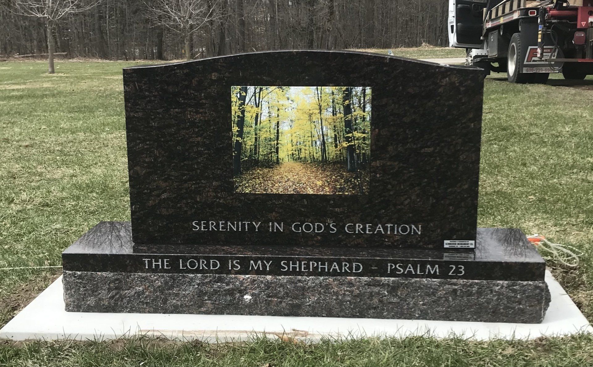 Black granite headstone with a forest scene and the Psalm 23 verse in a grassy setting.