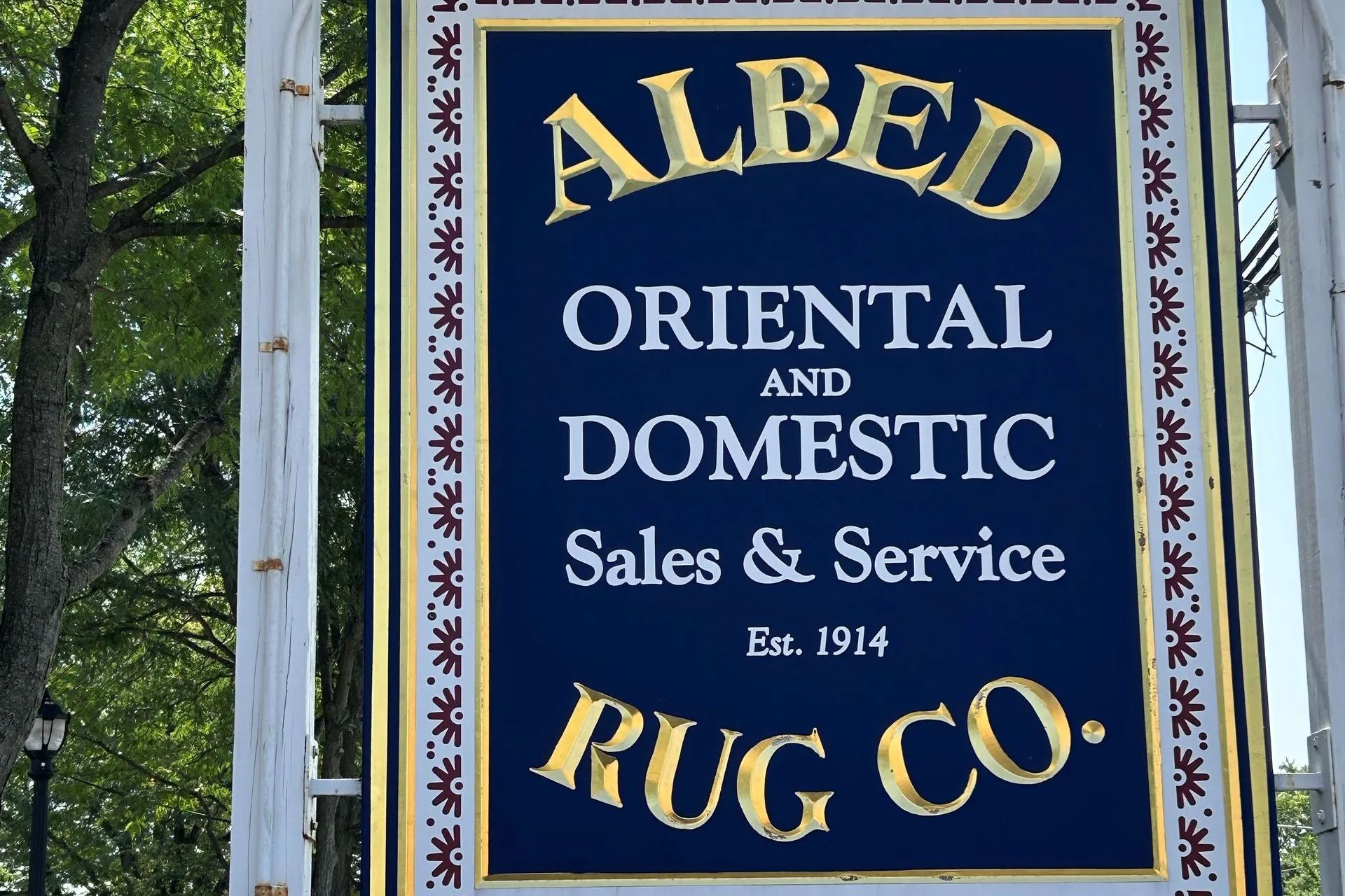 Sign for Albed Rug Co., with gold lettering on a navy blue background, bordered by a red and gold pattern.