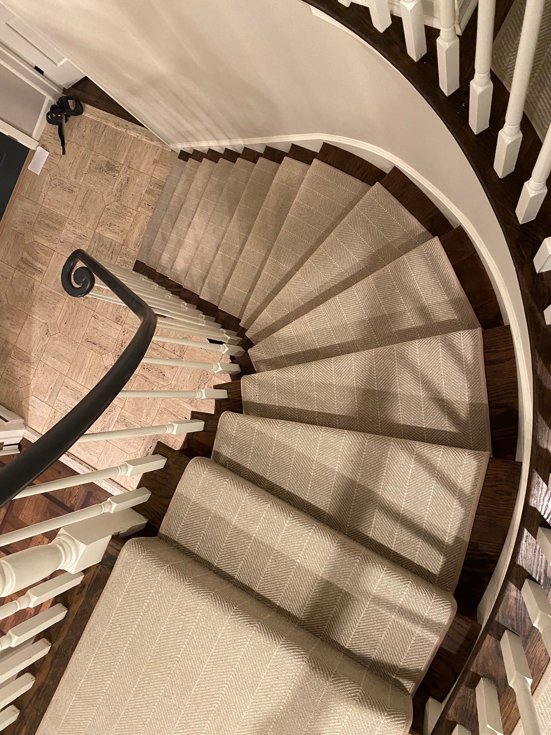 Curved staircase with beige carpet and white railing. Dark wooden steps are visible. A black handrail curves along the inner wall.
