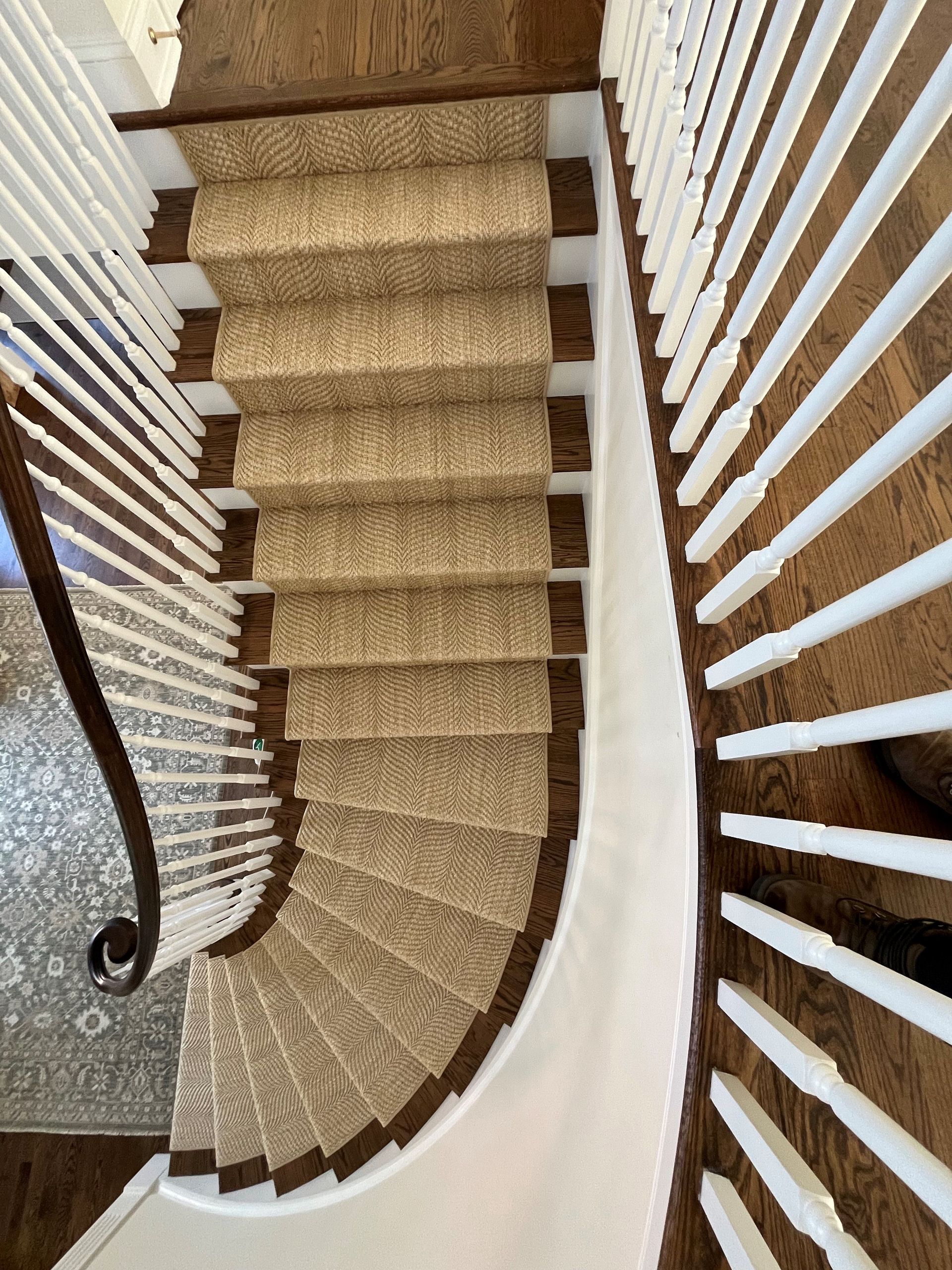 Overhead view of a curved staircase with beige carpet and white balusters, leading downwards.