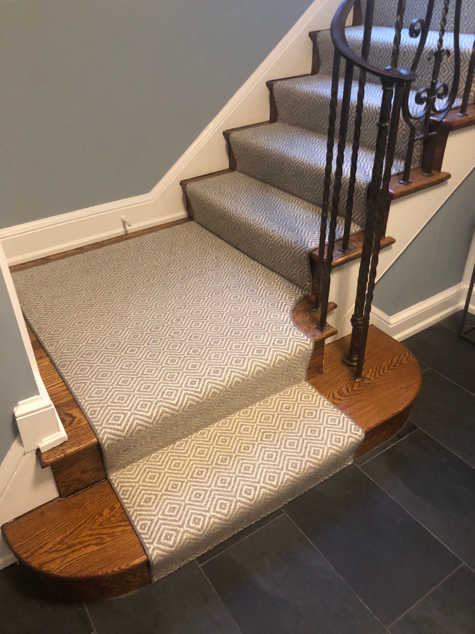 Carpeted staircase with wooden steps and a dark metal railing. The carpet is patterned in shades of gray and white.