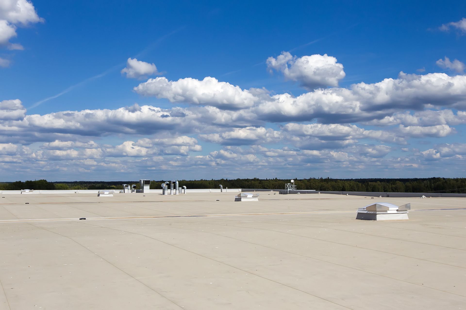 Large, beige industrial roof under a bright blue sky with puffy white clouds; distant trees on the horizon.
