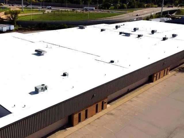 Aerial view of a large commercial building with a white roof and metal siding.
