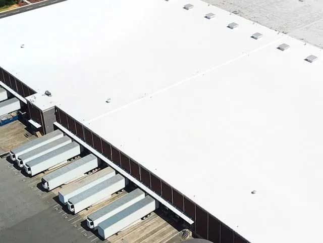 Overhead view of a white-roofed warehouse with docked semi-trailer trucks.