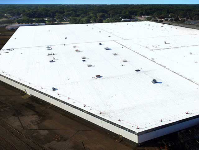 Large, white commercial building roof. Light-colored surface with multiple vents and a blue sky in the background.