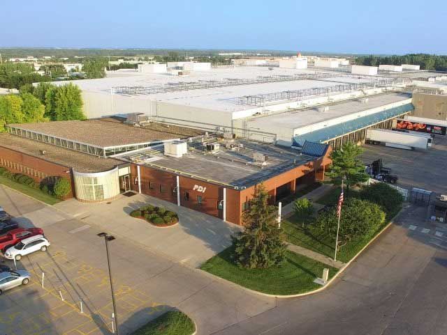 Aerial view of a large brick building with a loading dock and several parked trucks; clear blue sky.