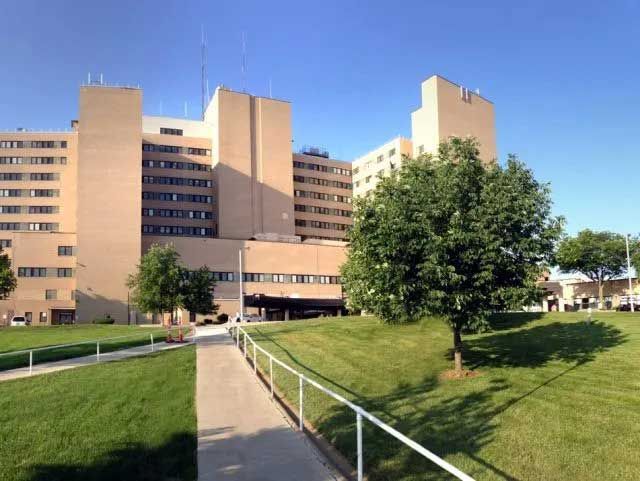 Hospital exterior, tan brick building with multiple stories, trees, and blue sky.