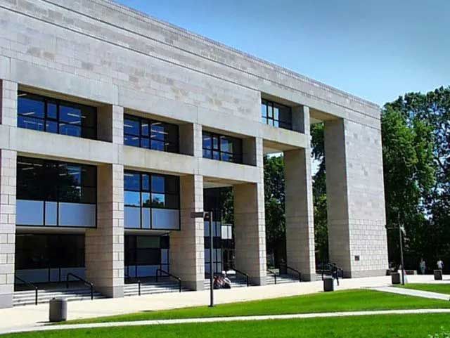 Large stone building with multiple windows and open archways, set on a grassy lawn.