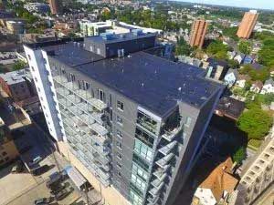 High-angle view of a modern apartment building with balconies, dark exterior, and surrounding urban landscape.