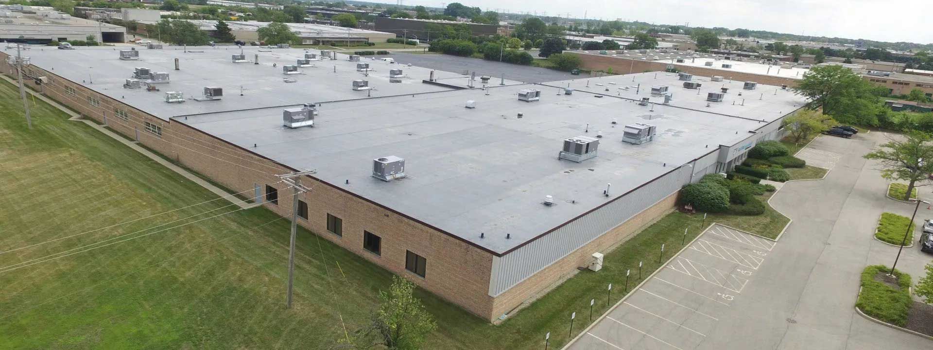 An aerial view of a large, flat-roofed commercial building with a surrounding green lawn and parking lot.
