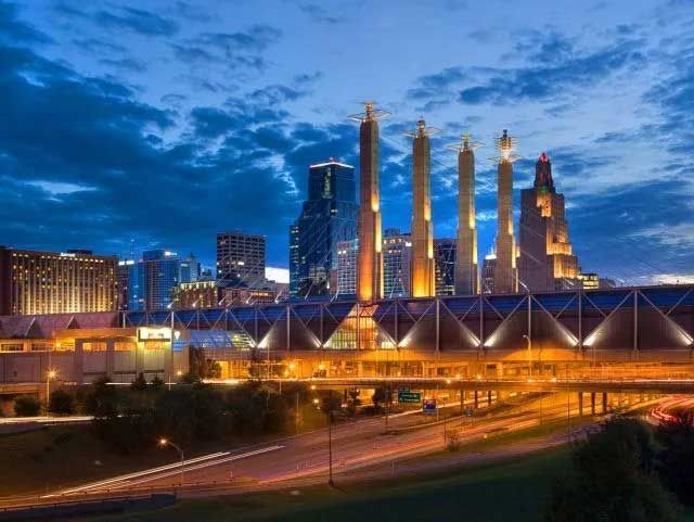 Kansas City skyline at dusk with lit buildings and towers under a blue sky.