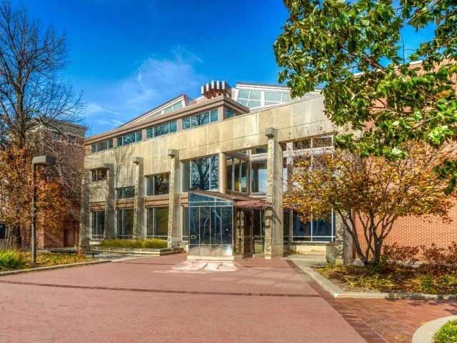 Modern building with glass entrance, brick facade, and trees under a blue sky.