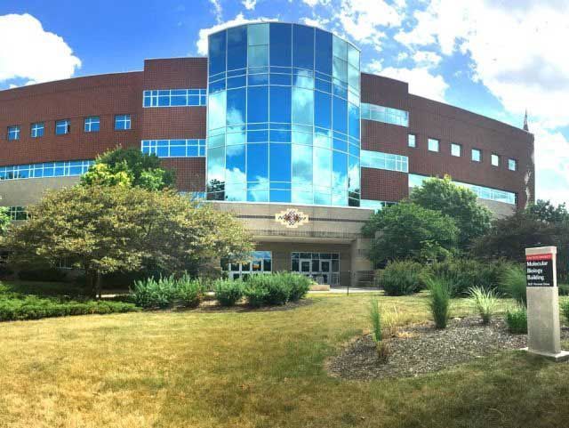 Brick building with glass entrance and windows reflecting sky. Sign in front.