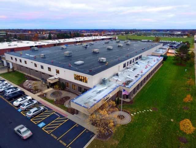 Aerial view of a large industrial building with a flat roof, surrounded by parking lots and green space.