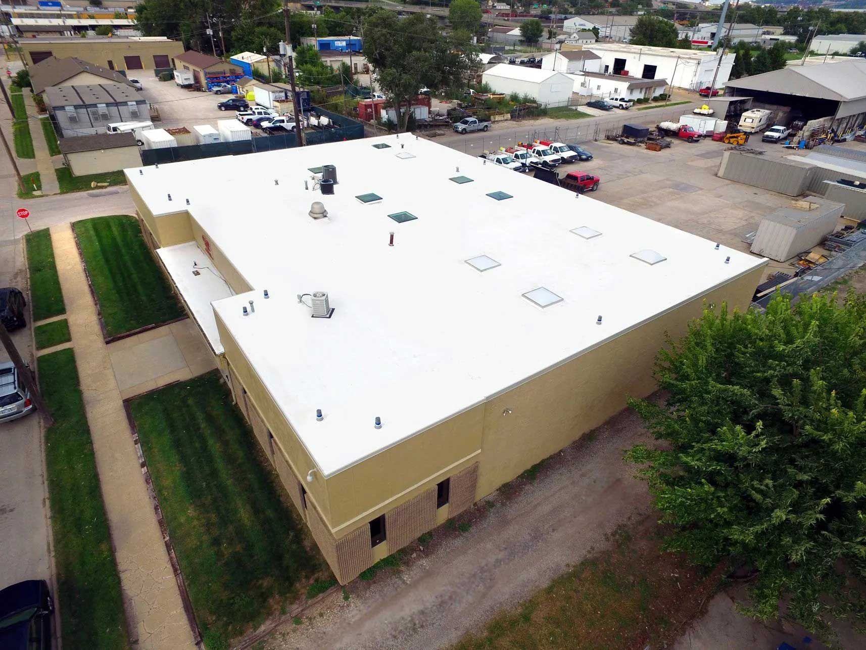 Overhead view of a tan commercial building with a white flat roof, green grass, and surrounding cityscape.