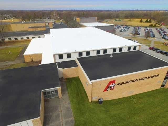 Aerial view of Assumption High School with white and black rooftops and a parking lot.