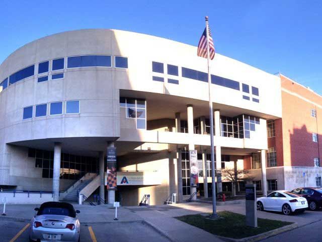 Building with a curved white facade, American flag, cars parked in front.
