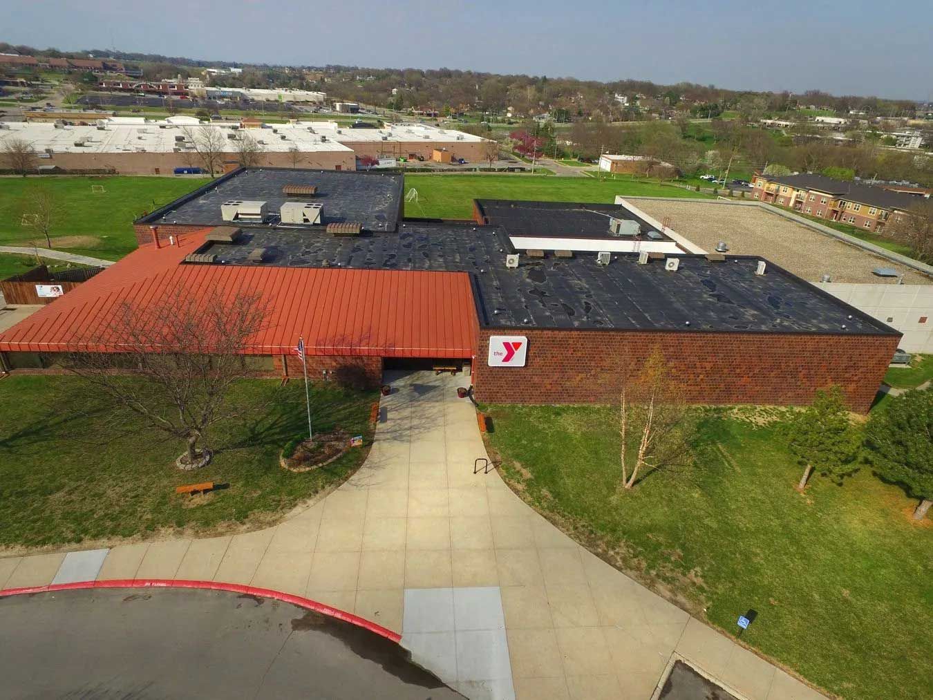 Aerial view of a YMCA building with a red roof, green lawn, and surrounding cityscape.