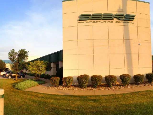 SERE Manufacturing company building with green and beige facade, landscaping, and parked vehicles.