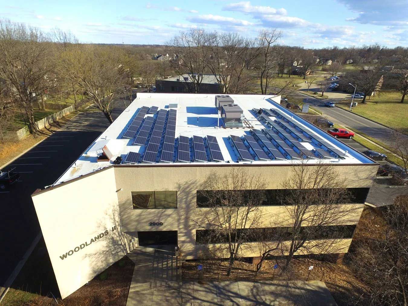 A building with a flat roof covered in solar panels, trees surround.