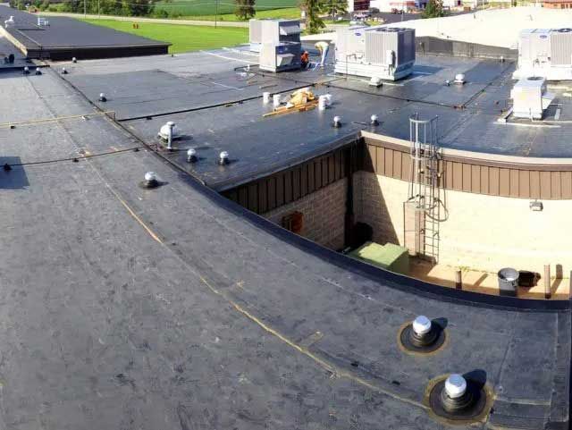 A black flat roof with HVAC units, a ladder, and circular features on a building.