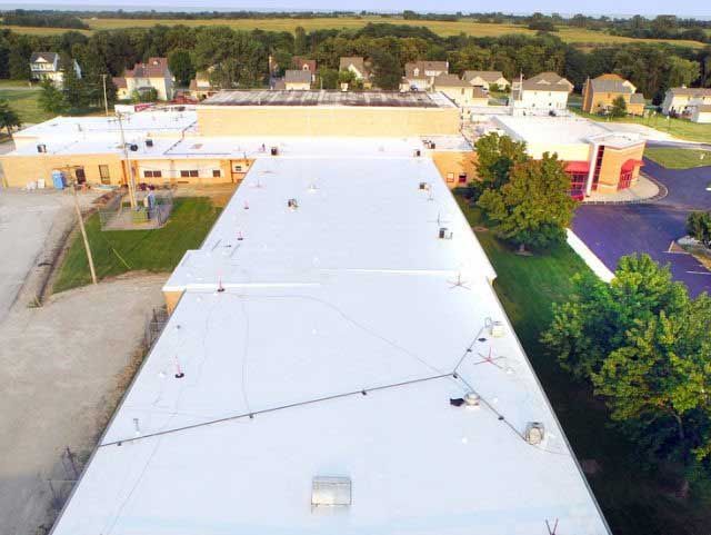 Aerial view of a long white commercial roof, trees, and buildings in the background.