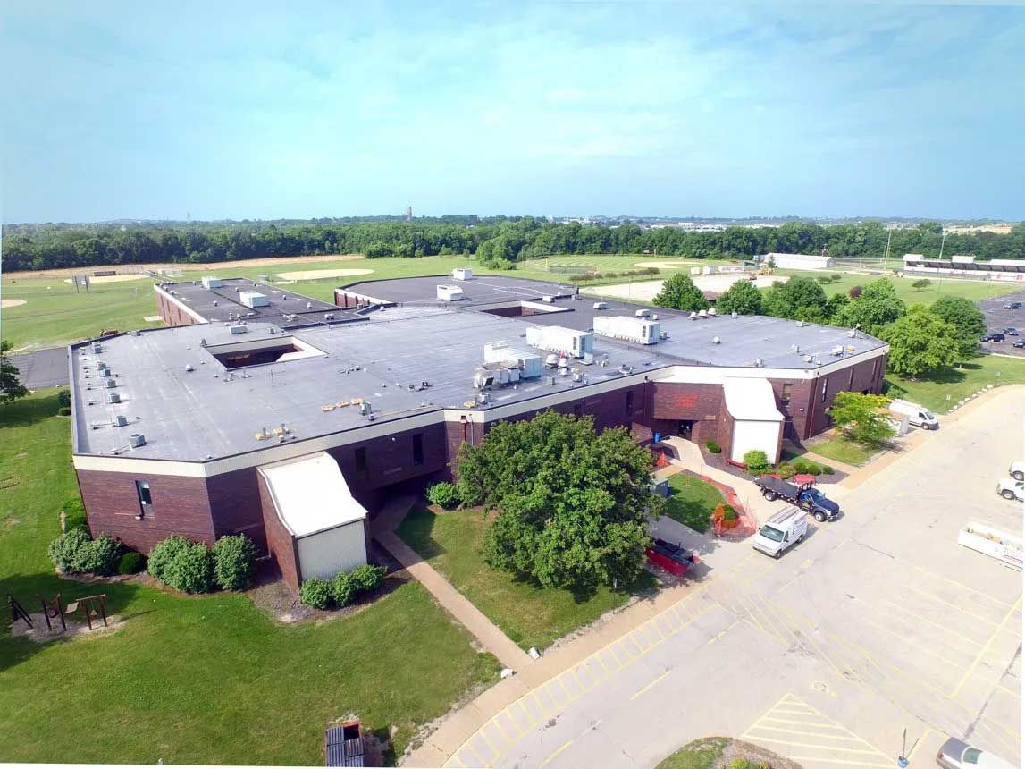 Aerial view of a brown brick building with a flat roof, surrounded by green grass and a parking lot.