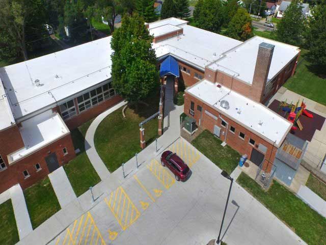 Aerial view of a red brick school building with a car parked outside and playground equipment.