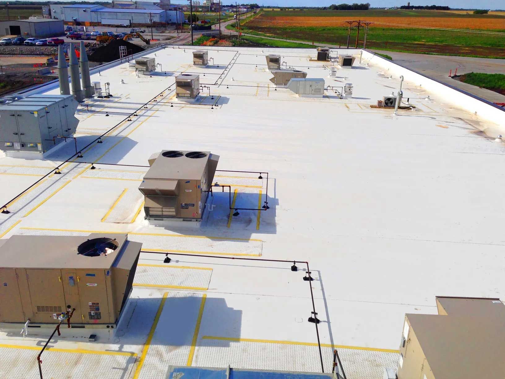 White commercial building rooftop with HVAC units and piping, against a field.