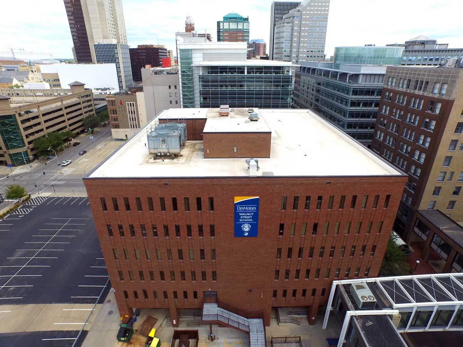 Brick building in city; blue banner, rooftop equipment, surrounding buildings and parking area visible.