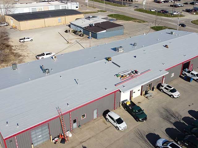 Aerial view of a commercial building with a gray roof and several vehicles parked outside.