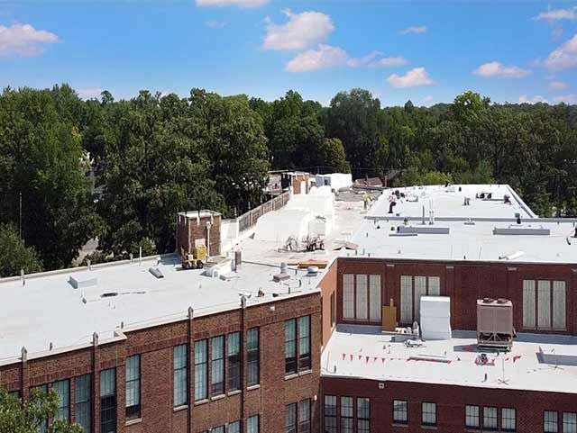 Aerial view of a school roof under construction with workers and equipment on a sunny day.