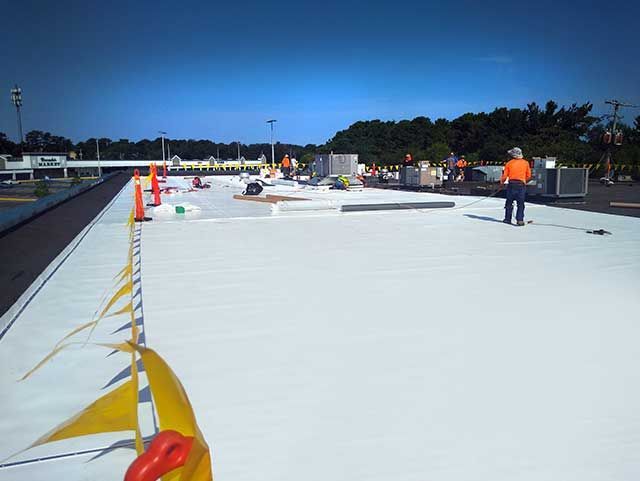 Construction workers on a white, flat commercial roof; setting up safety barriers and equipment.